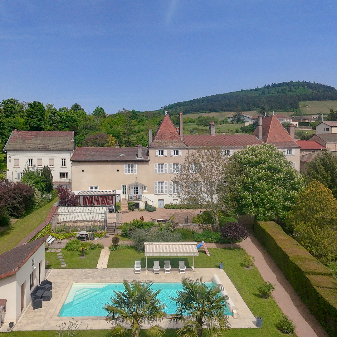 Vue aérienne d'une maison bourgeoise de 1821 avec piscine chauffée, parc arboré et rivière à La Roche-Vineuse en Bourgogne du Sud.