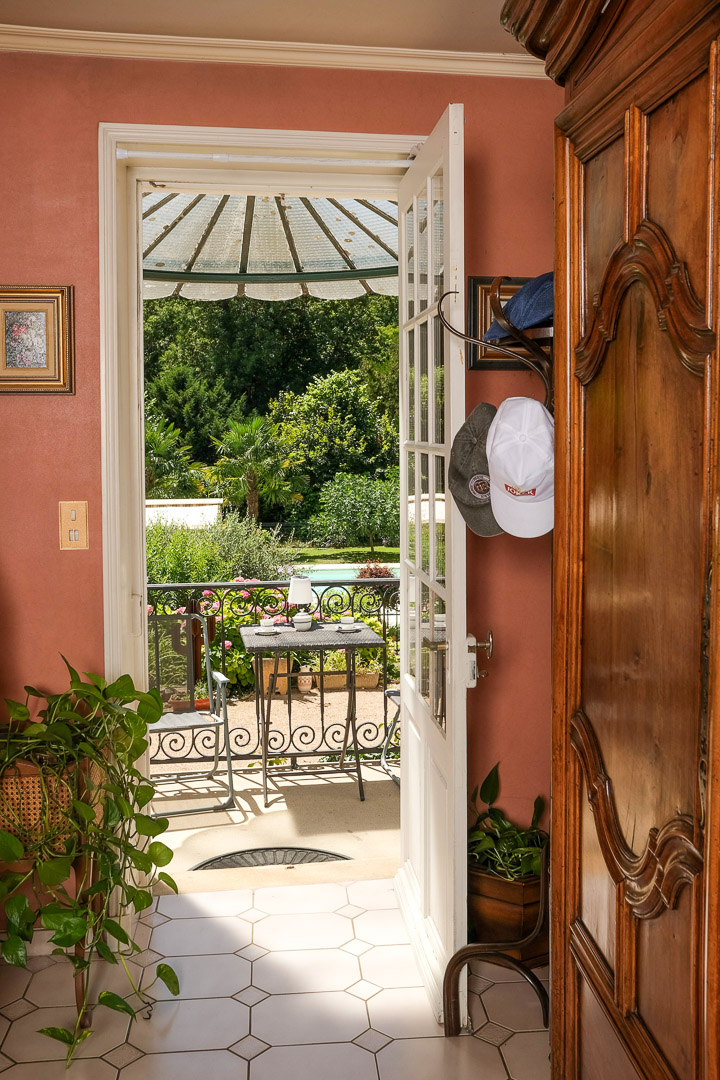 Vue intérieure ouvrant sur une terrasse, la piscine chauffée et le parc arboré d'une demeure bourgeoise à La Roche-Vineuse.