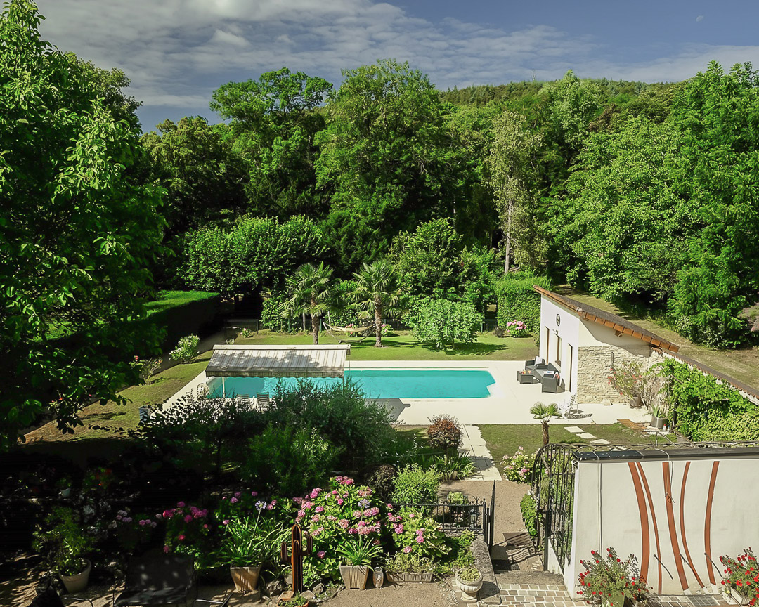 Vue dominante sur la piscine chauffée, le salon d'été et le parc arboré d'une demeure de caractère à La Roche-Vineuse.