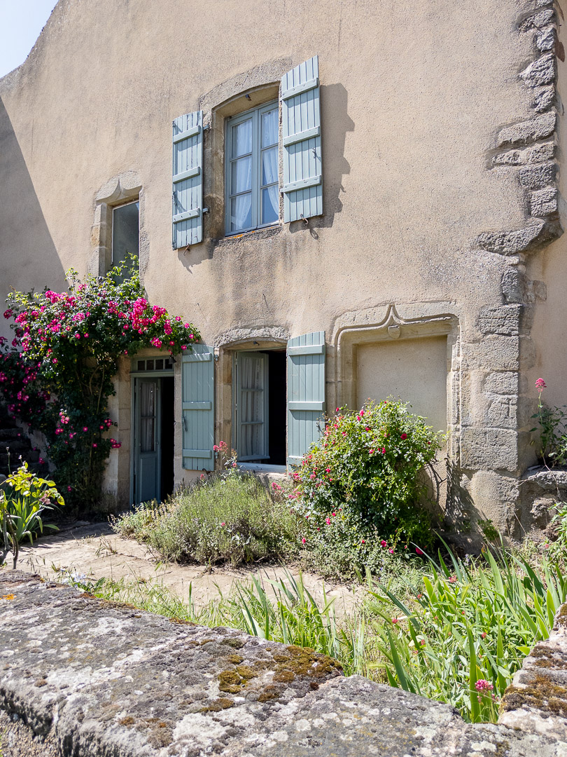 Façade principale d'un ancien presbytère du XIVe siècle avec jardin clos, rosiers anciens et volets bleu grisé à Gourdon en Bourgogne du Sud.