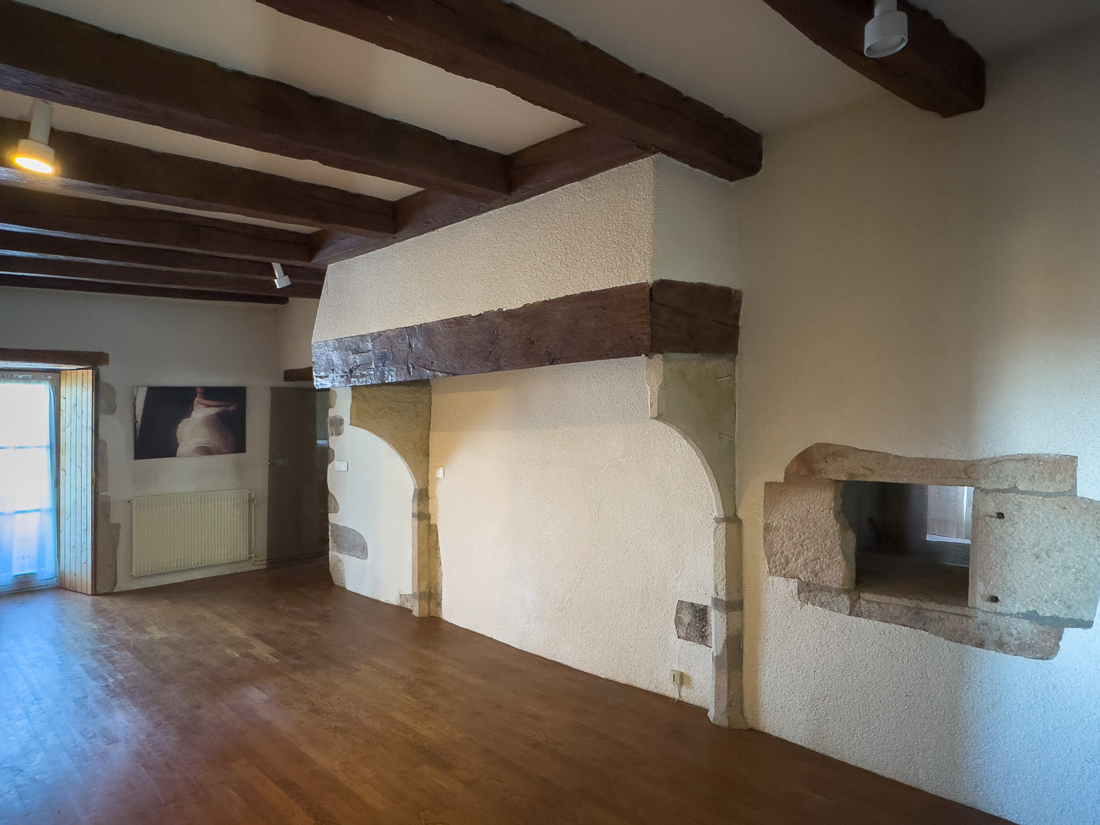 Grande pièce avec poutres apparentes et cheminée ancienne dans un presbytère en Bourgogne