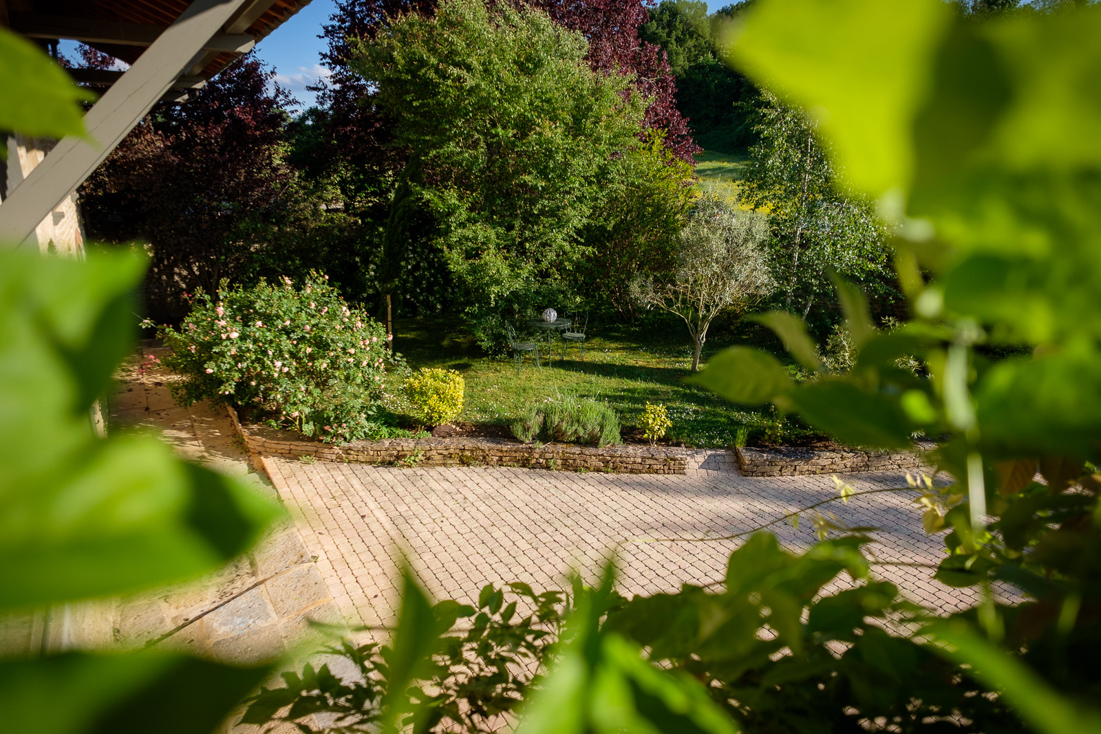Vue sur jardin arboré et cour pavée dans propriété de caractère rénovée en Bourgogne du Sud