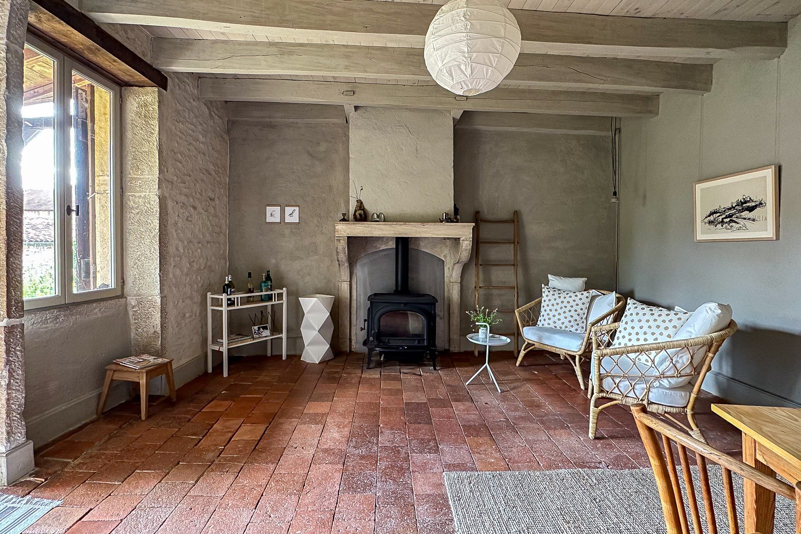 Salon avec cheminée en pierre, tomettes et poutres apparentes dans une maison bourguignonne