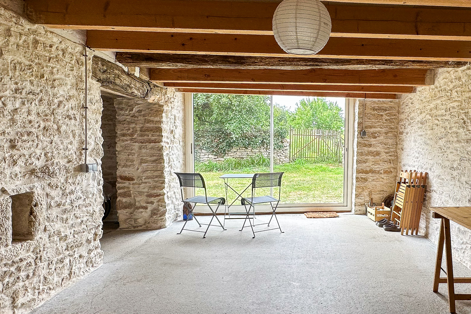 Grande pièce en pierre avec baie vitrée donnant sur le jardin dans une maison de campagne bourguignonne