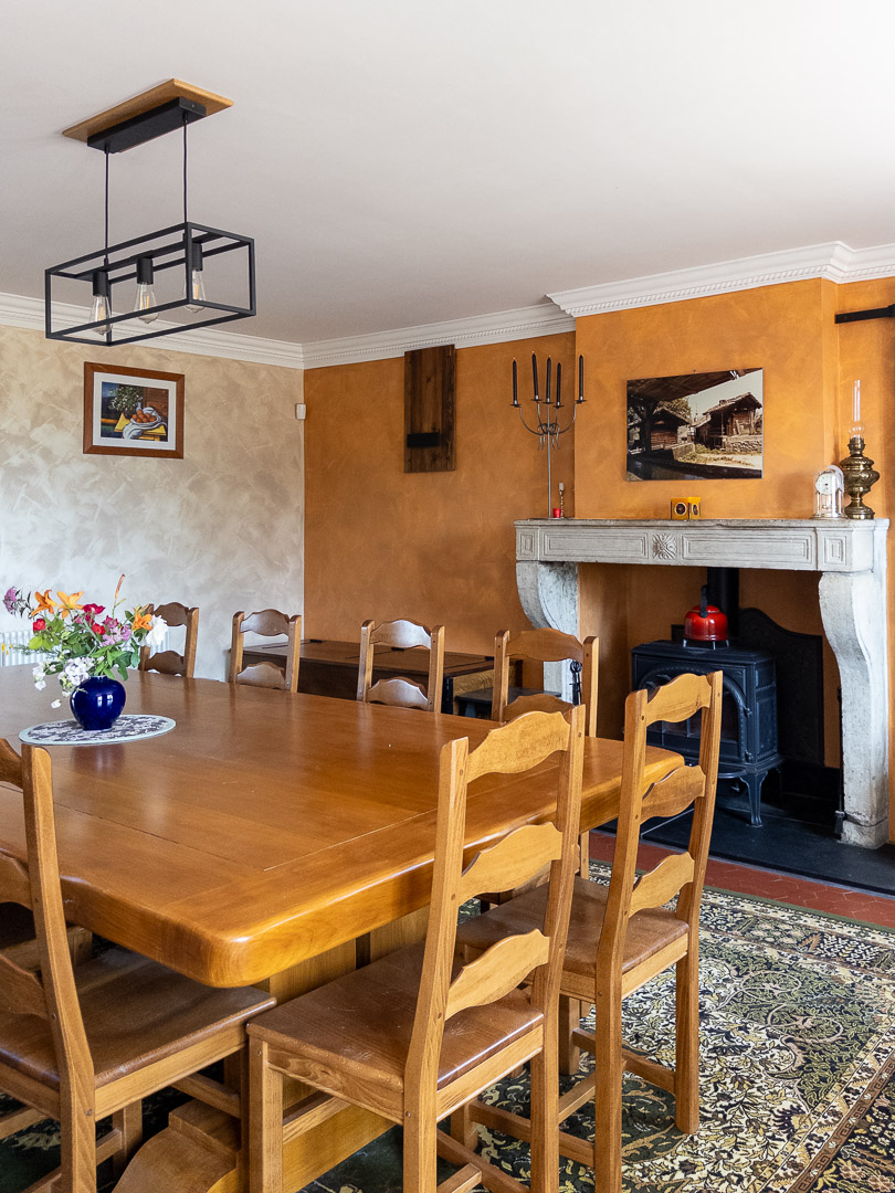 Salle à manger avec cheminée en pierre, poêle à bois et grande table familiale.