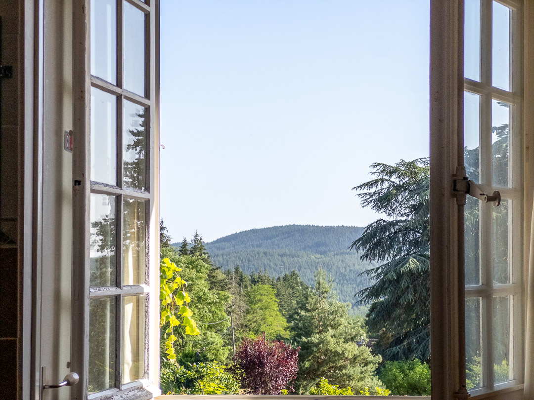 Vue depuis une chambre sur les collines boisées et le parc arboré d'une propriété de caractère à Ozolles.