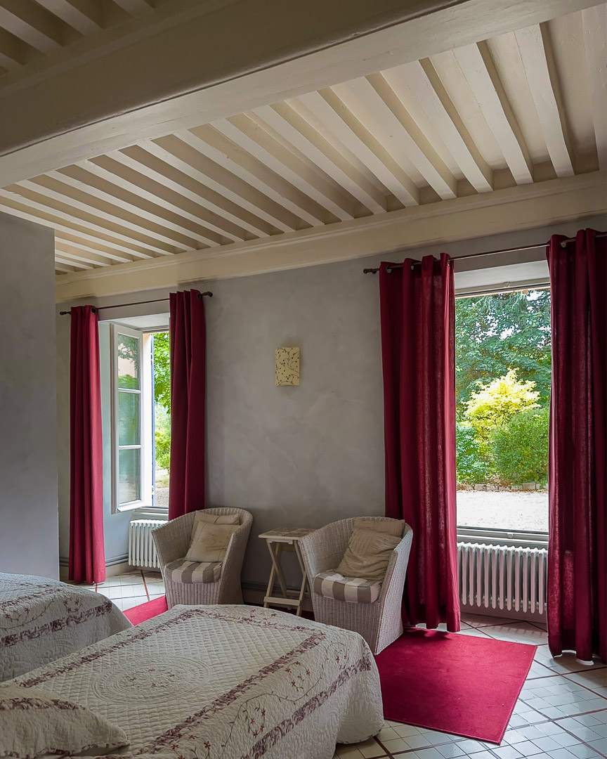 Chambre de plain-pied avec poutres apparentes et vue sur le jardin dans une maison bourgeoise du XVIIIᵉ siècle en Clunisois.