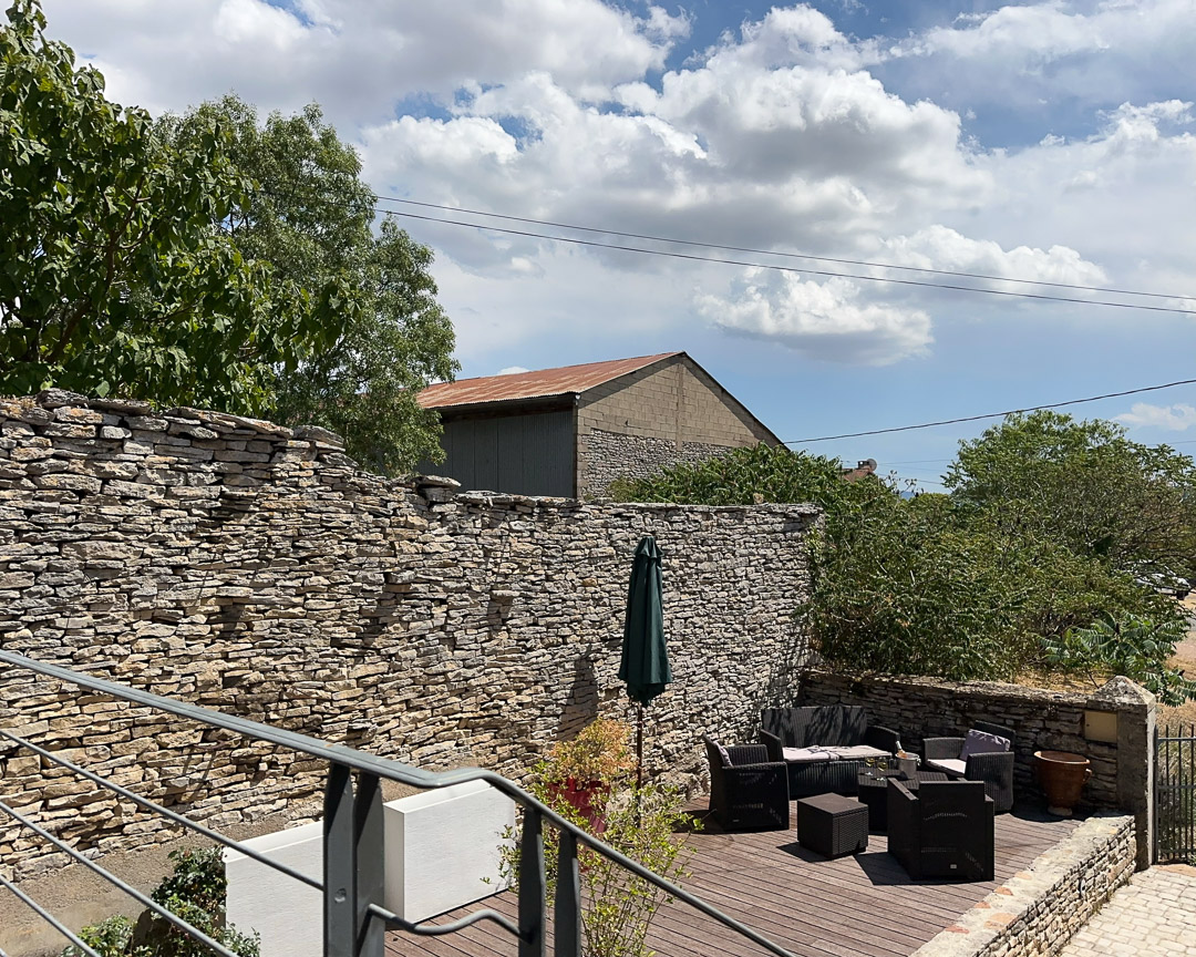 Cour close entourée de murs en pierre et terrasse en bois dans une maison de caractère à Cortevaix, entre Cluny et Salornay-sur-Guye.