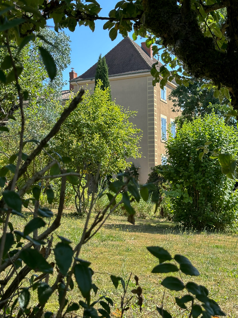 Façade d'une maison bourgeoise du XVIIIᵉ siècle aperçue à travers les arbres de son jardin dans le Clunisois.