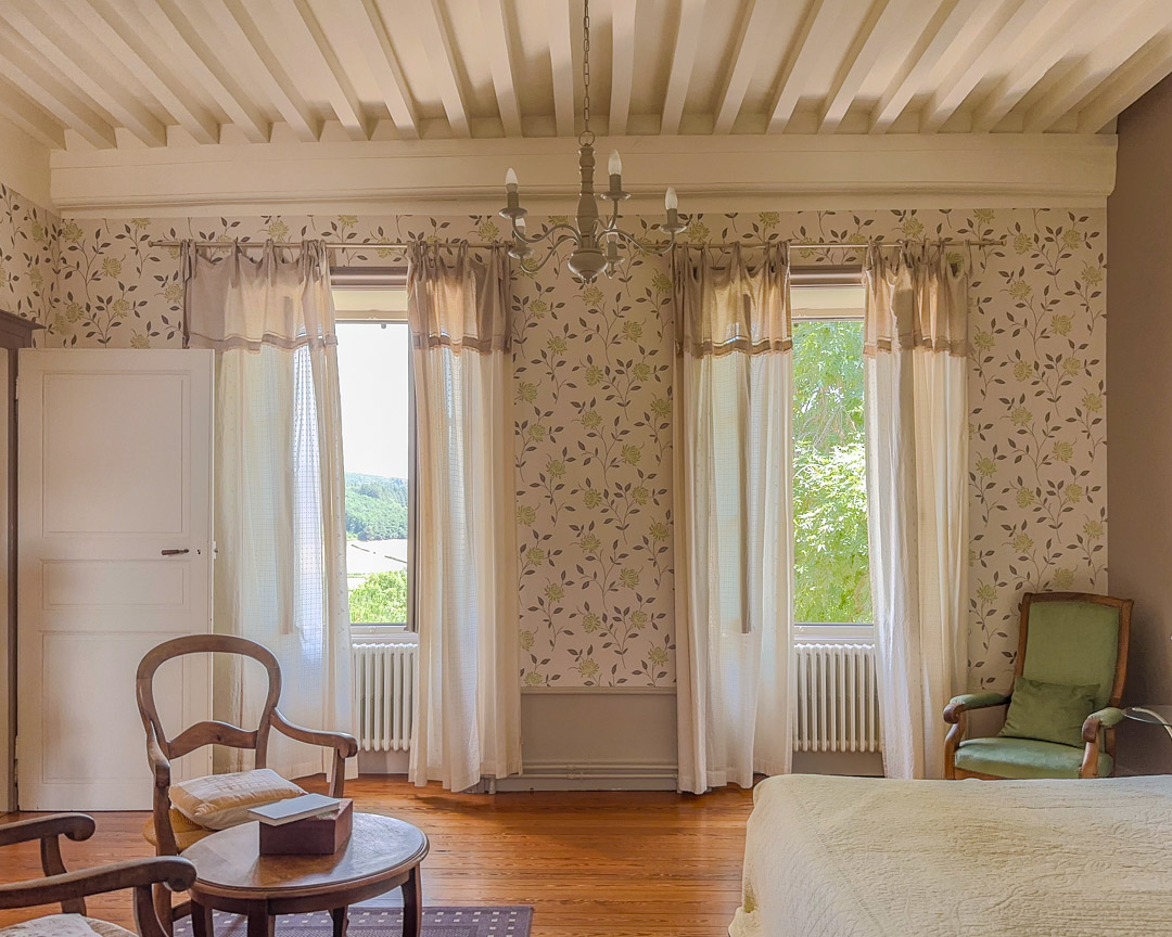 Grande chambre avec plafond à la française et fenêtres ouvertes sur le jardin dans une maison bourgeoise du XVIIIᵉ siècle en Clunisois.