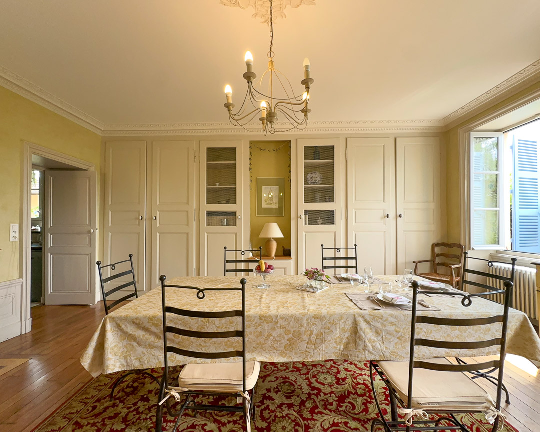 Salle à manger de réception d'une maison bourgeoise du XVIIIᵉ siècle dans le Clunisois, avec boiseries, parquet, cheminée ancienne et vue sur le jardin.
