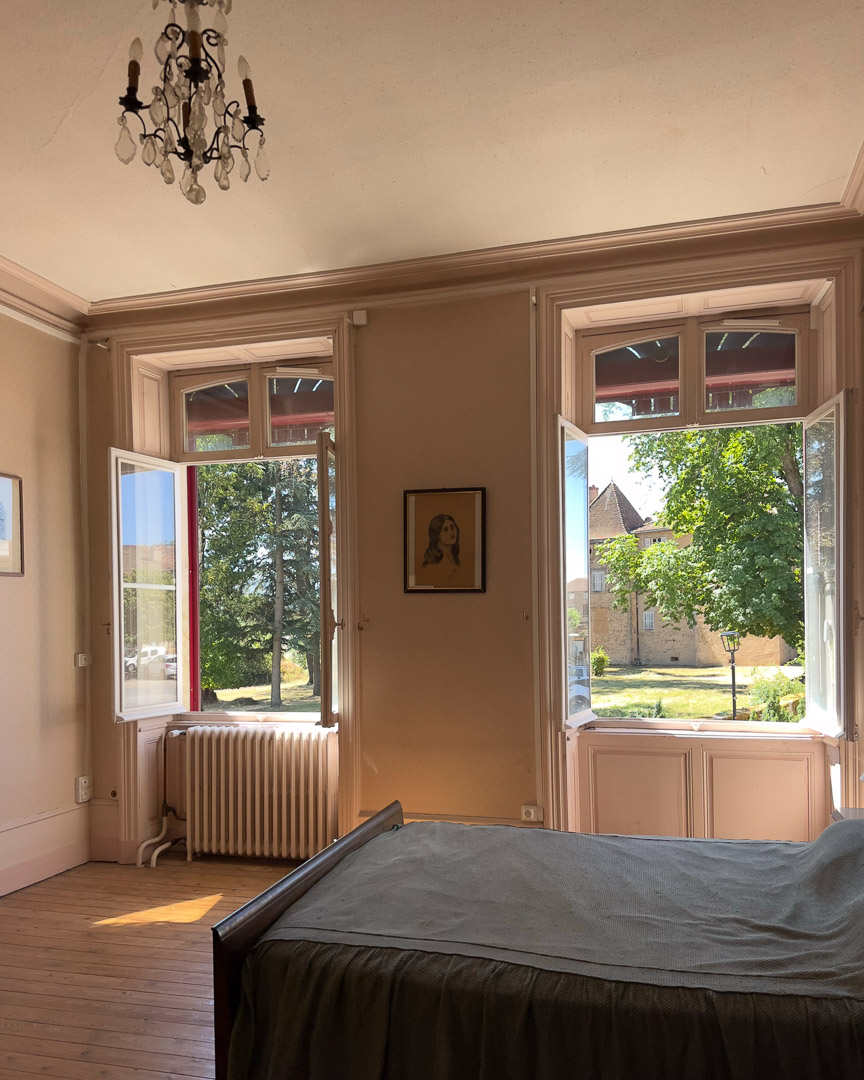 Grande chambre lumineuse avec vue sur le château de Tramayes dans une ancienne demeure bourgeoise.