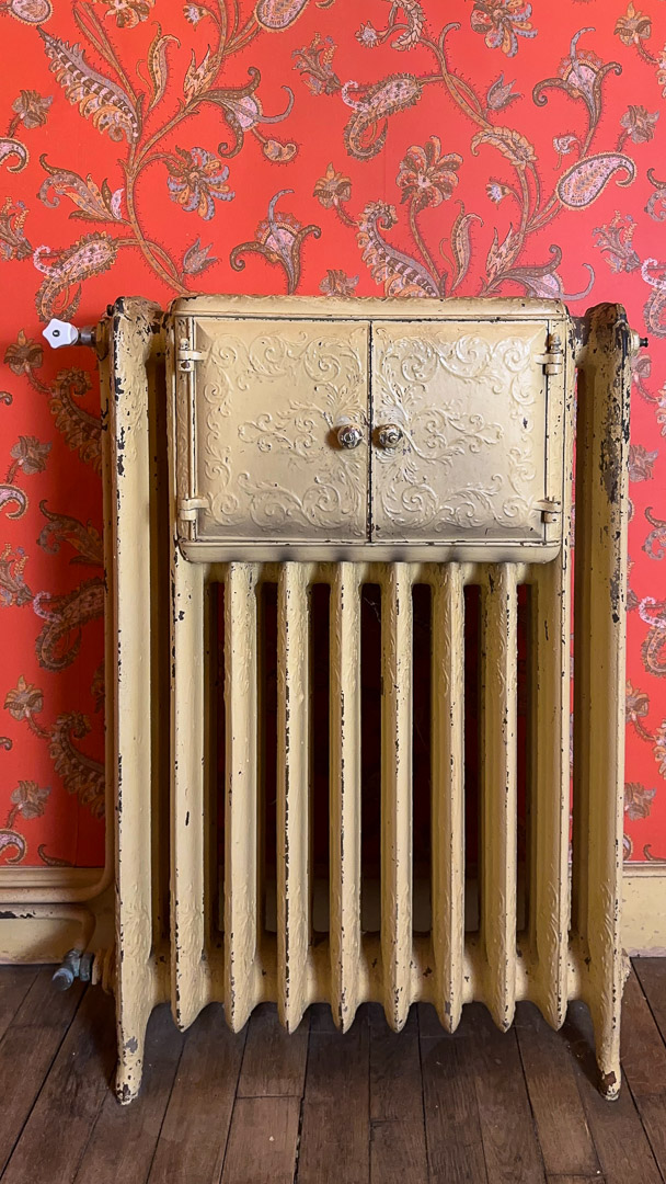 Radiateur ancien en fonte avec potager intégré devant un papier peint d'époque dans une demeure bourgeoise à Tramayes.