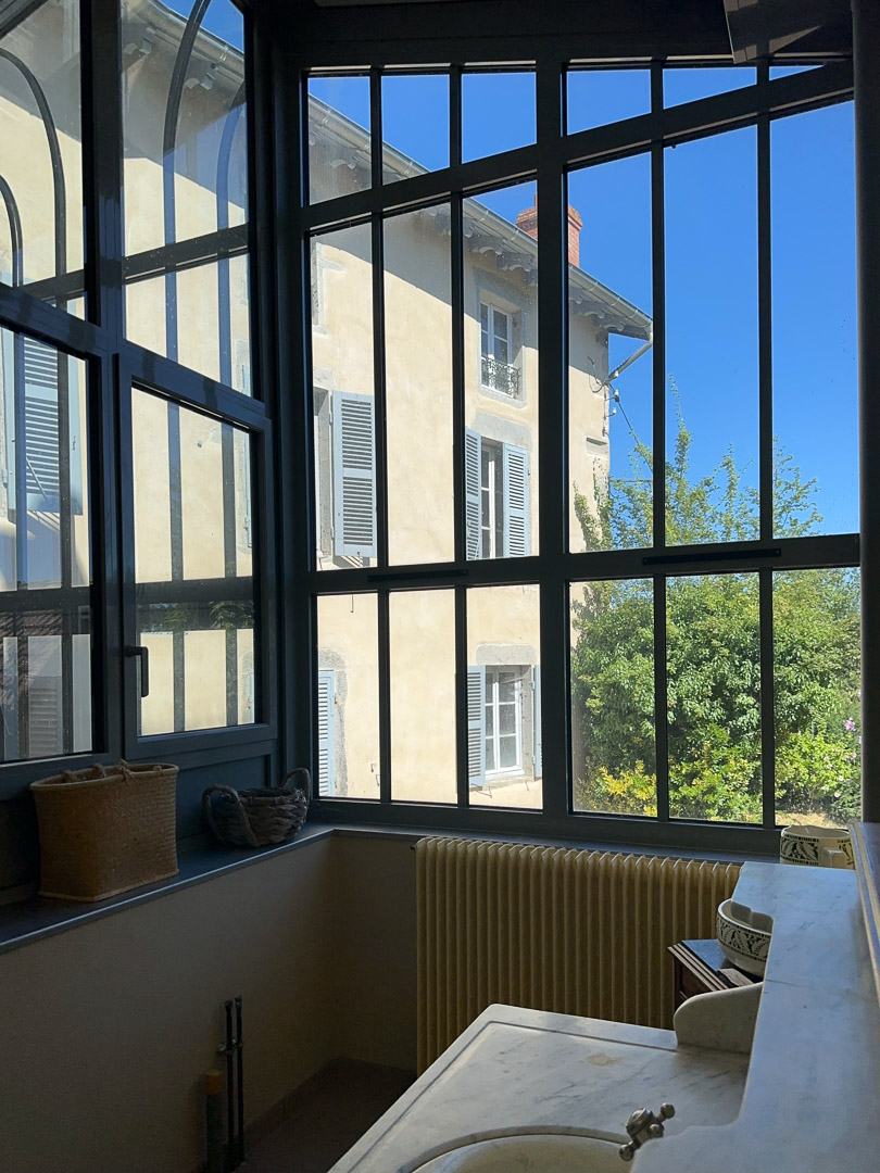 Vue sur le jardin depuis l'arrière-cuisine à travers une verrière contemporaine dans une demeure bourgeoise à Tramayes.