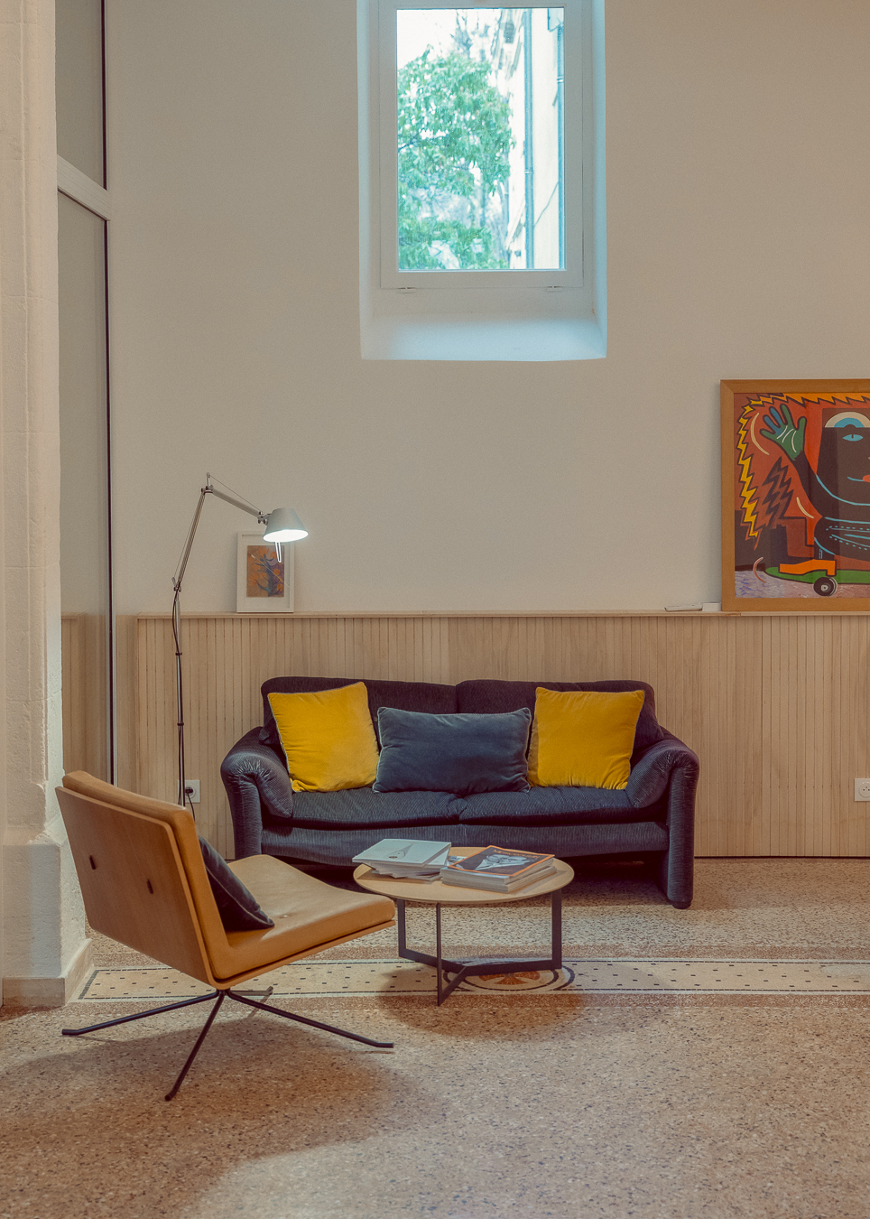 Salon avec canapé, fauteuil, table basse, œuvres d’art et sol en terrazzo dans une ancienne chapelle à Montpellier.