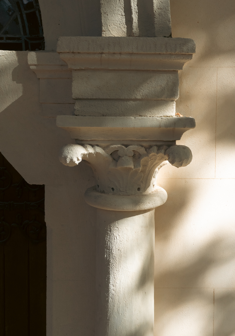 Chapiteau sculpté et colonne d’une ancienne chapelle à Montpellier, éclairés latéralement par une lumière filtrée par les arbres.