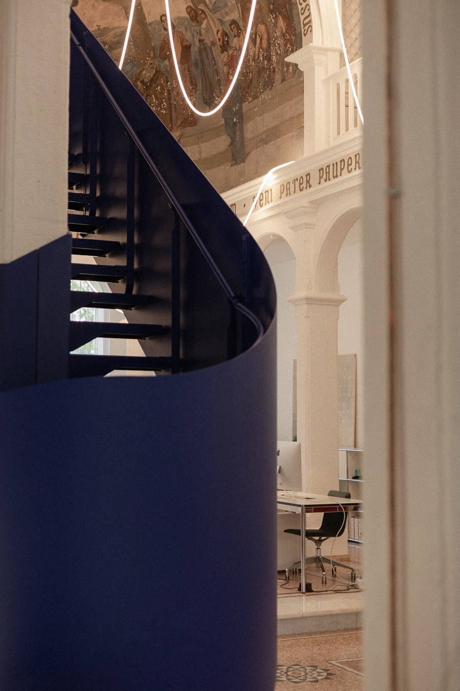 Escalier bleu sculptural cadré entre les éléments blancs d’une ancienne chapelle, avec décor peint et suspension lumineuse à Montpellier.