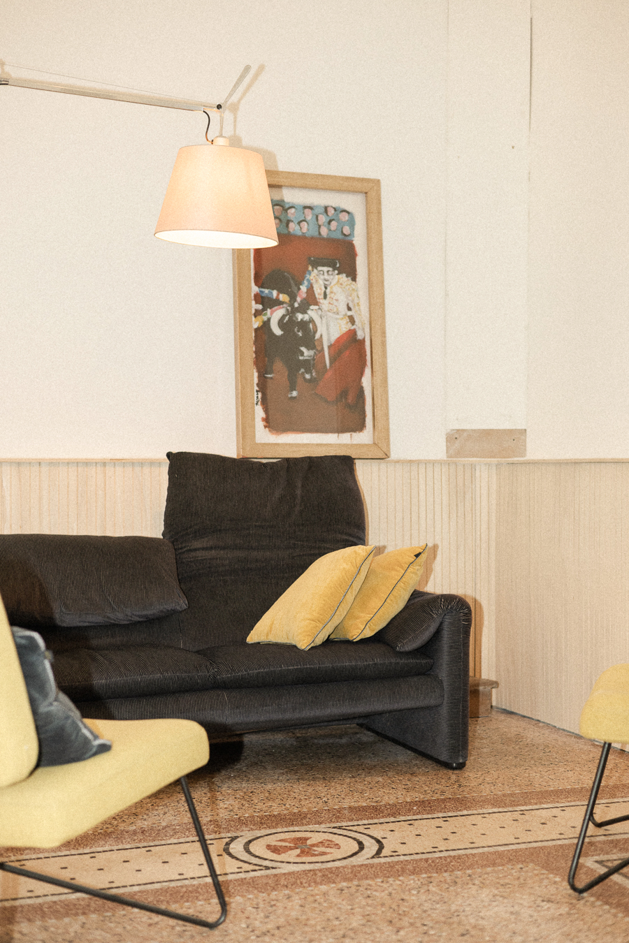 Salon contemporain avec canapé sombre, fauteuils jaunes, œuvre d’art et sol en terrazzo dans une ancienne chapelle à Montpellier.