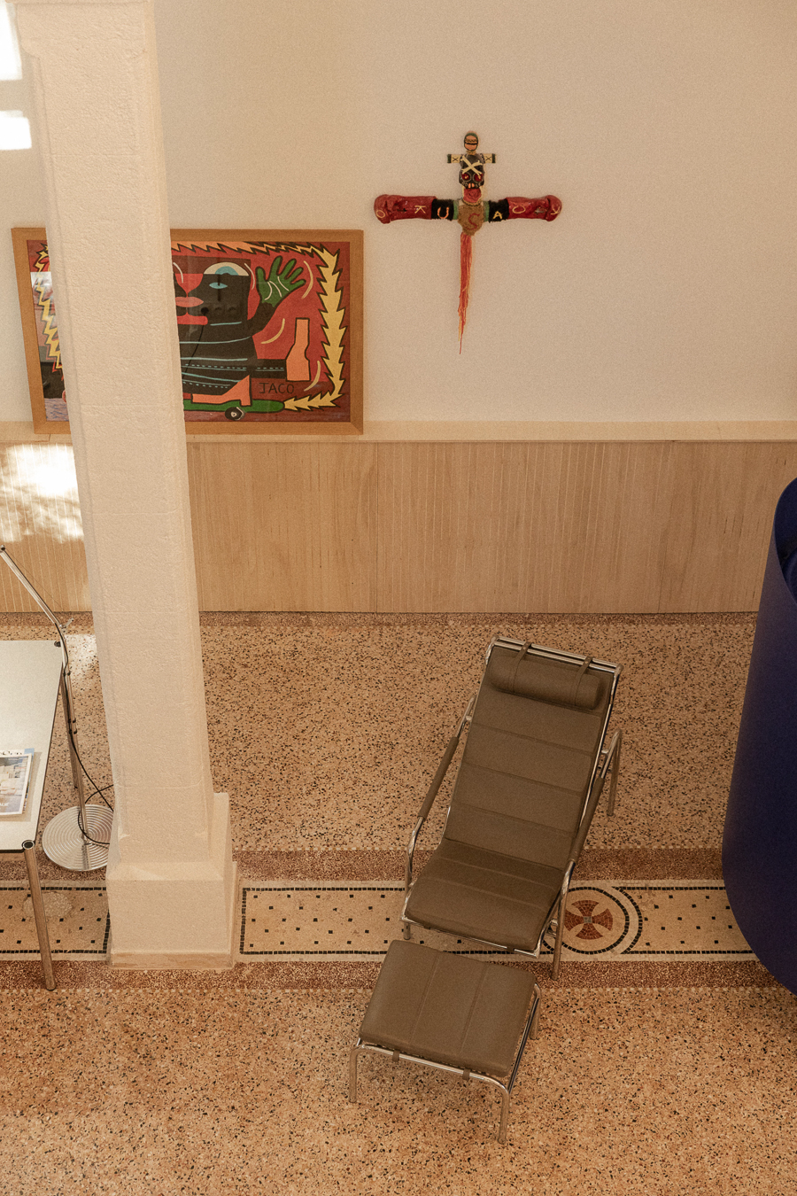 Vue en plongée sur un sol en terrazzo, une colonne, une chaise longue et des œuvres contemporaines dans une ancienne chapelle à Montpellier.